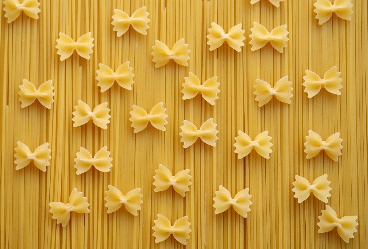 Flat lay of Italian pasta varieties, showcasing farfalle and spaghetti on a neutral background.